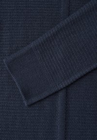 Dunkelblaues Strickkleidungsstück mit einem strukturierten Muster, das über ein geripptes Bündchen verfügt. Der Stoff wirkt weich und flexibel, was Komfort und Wärme betont.