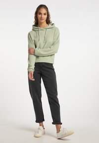 Felpa verde chiaro, con texture, dotata di cappuccio e cordini, abbinata a jeans neri con risvolto e sneakers bianche. Design semplice e casual.