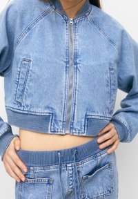 Lichtblauwe denim bomberjack met een cropped ontwerp, geribbelde mouwen en tailleband. Bevat een ritssluiting aan de voorkant en twee voordozen.