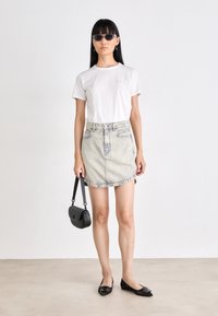 Witte katoenen t-shirt, lichtblauwe denim minirok, zwarte platte schoenen en een kleine zwarte handtas. Model met een zonnebril en lang haar.
