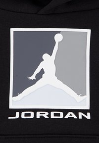 Hoodie noir avec un logo "Jumpman" blanc prominent dans une boîte grise et blanche. Le texte en dessous indique "JORDAN" en lettres blanches en gras.