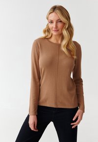 Tricou lung cu mânecă maro, dintr-un material moale și texturat, cu guler rotund și detalii cusute, asortat cu blugi închisi la culoare.