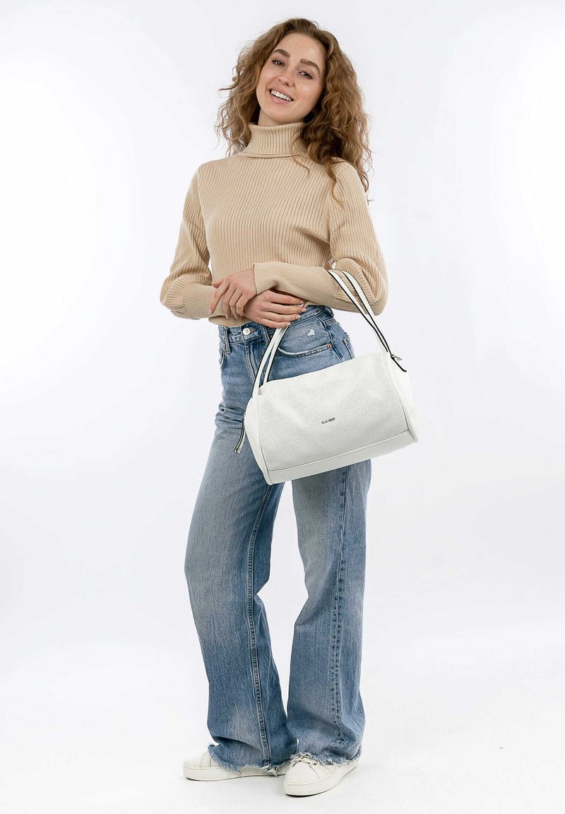 Weißer strukturierter Handtasche mit schwarzen Akzenten, runder Form und doppelten Griffen. Modell trägt einen beigefarbenen gerippten Pullover und hellblaue Jeans.