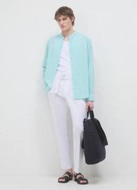 Chemise boutonnée bleu clair, pantalon blanc, sandales noires, tenant un sac sombre. Tissu léger, coupe décontractée et col rond.