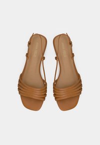 Paire de sandales plates en cuir marron clair avec plusieurs brides à l'avant et fermetures à boucle à la cheville, vues de dessus sur un fond blanc.