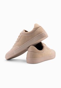Béžové semišové tenisky s klasickým designem, kulatou špičkou, texturovaným povrchem a gumovými podrážkami s jemnými vzory a detaily tkaniček.