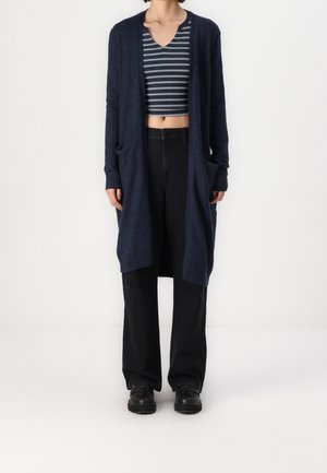 Granatowy sweter kardigan z dzianiny z długimi rękawami, otwartym przodem i bocznymi kieszeniami, w zestawieniu z paskowanym topem crop i czarnymi spodniami o szerokich nogawkach.