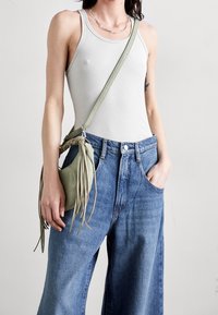 Top de tirantes acanalado gris claro, pantalones de mezclilla azul de tiro alto y un pequeño bolso cruzado de cuero verde con detalles de flecos.