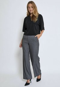 Black short-sleeve top with vertical stripes paired with high-waisted gray wide-leg pants, worn with black pointed heels.