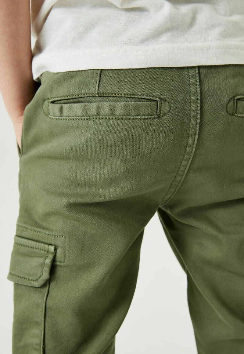 Grüne Cargo-Hosen aus strapazierfähigem Material, mit Gesäßtaschen und lockerer Passform, sichtbaren Nähten und einer glatten Textur.