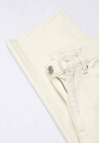 Jeans in denim color crema con orli sfrangiati, chiusura a zip e un bottone argentato come dettaglio. Piegati piatti, mostrando la texture e una sottile venatura.