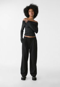Sort off-the-shoulder top i tekstureret stof, parret med løse sorte bukser med frontknap og sidelommer. Sorte platform sko.