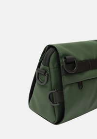 Borsa a tracolla verde con superficie testurizzata, dotata di hardware nero e clip laterali. Il design angolare include una tasca con zip.