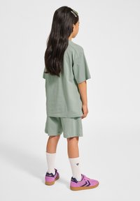 Grön bomullströja och shorts-set, med korta ärmar, matchat med rosa träningsskor, vita strumpor och hårspännen i mörkt hår.