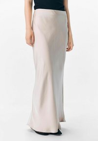 Lange, beige satijnen rok met een soepele textuur, voorzien van een strak zittende taille en een lichte flare aan de zoom, gedragen met een zwarte top en schoenen.