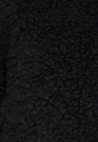 Czarna tkanina polarowa o teksturowanej, puszystej powierzchni. Materiał wygląda na gruby i ciepły, z kręconym, wełnianym wzorem.