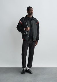 Must musternokaga musternokaga murrugaäinenulukate mustüstus, millele on lisatud punased ja valged triibud, musta sviitri, hallide pükste ja mustade lohvidega kaetud. Väike õlakott aksessuaarina.