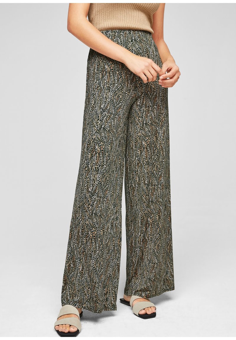 Personne portant un pantalon large à taille haute à motifs noir, beige et blanc, un haut sans manches beige et des sandales ouvertes beige.