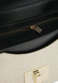 Borsa a mano in tela bianca con finiture in pelle nera, caratterizzata da una chiusura e una cerniera dorate. L'interno è foderato in nero, con dettagli di cucitura visibili.