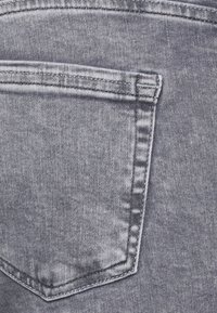 Tecido de denim cinza com um bolso traseiro com aba pontiaguda, costura visível e uma textura subtil sem padrões ou detalhes.
