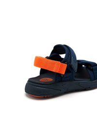 Sandale bleue avec une sangle orange réglable. Présente un dessus texturé, une semelle en caoutchouc et une semelle intérieure rembourrée pour le confort.