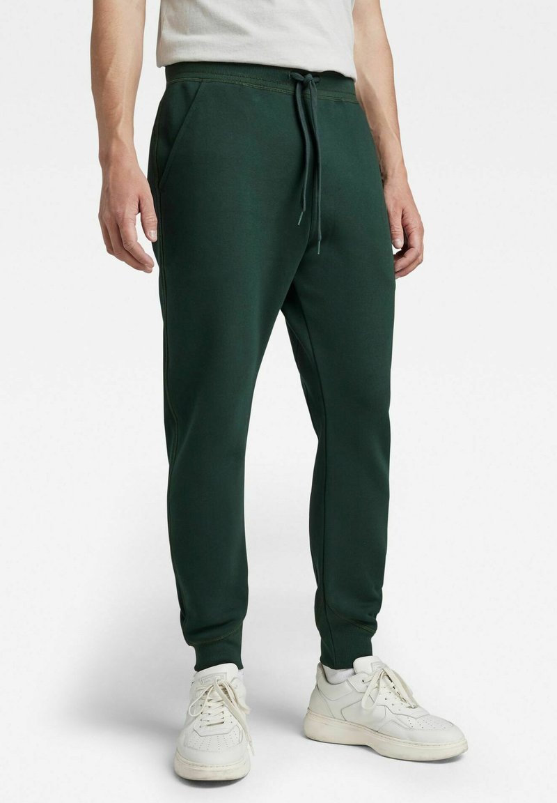 Pantalones deportivos de color verde oscuro con cintura elástica y cordón. Cuenta con bolsillos laterales y piernas ajustadas. Material de mezcla de algodón.
