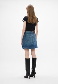 Denim-Minirock mit schwingendem Schnitt, hellblauer Waschung, hinten aufgesetzten Taschen und braunem Lederakzent an der Taille. Schwarze kniehohe High Heels Stiefel.
