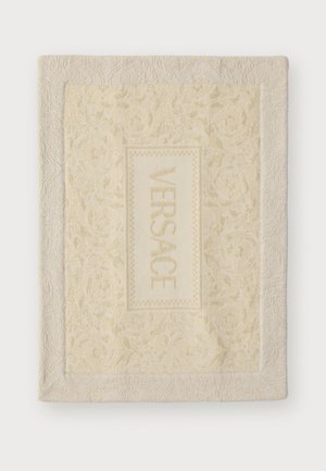 Versace blanket in soft cream with an embossed floral pattern, featuring a rectangular logo patch in lighter cream centered on the fabric.