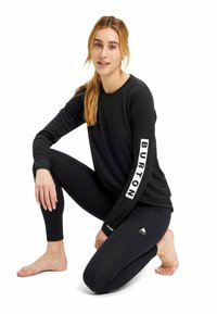 Maglietta nera a maniche lunghe con logo "BURTON" sulla manica, abbinata a leggings neri. Texture liscia, design aderente. Nessun motivo o accento.