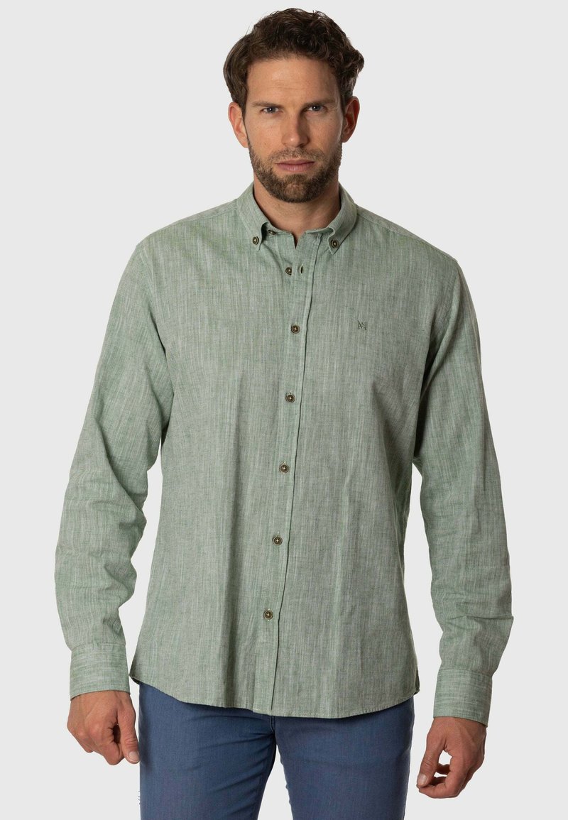 Camisa de botones verde claro con una tela texturizada, que presenta un pequeño logo bordado y botones marrones, llevada sobre pantalones azules.