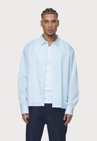 Svetlo modrá pruhovaná košeľa s dlhým rukávom vyrobená z bavlnenej látky, s button-down dizajnom, vo voľnom strihu a vyšívaným logom na hrudi.