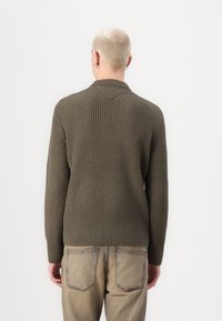 Olíva zöld bordázott kötött pulóver V-nyakú gallérral, hosszú ujjal és szabott derékkal. A textúrált anyag mélységet és érdeklődést ad.