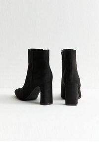 Las botas de tobillo de ante sintético negro cuentan con un tacón cuadrado, punta redondeada y cierre de cremallera lateral, exhibiendo una textura suave y un diseño elegante.