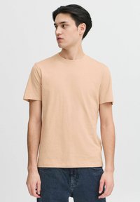 Light beige short-sleeve t-shirt in a soft cotton blend, featuring a crew neck and a relaxed fit. Paired with dark denim jeans.