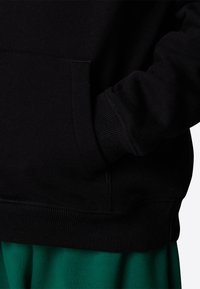 Felpa nera con cappuccio, con orlo e polsini a coste, dotata di tasca frontale e una finitura morbida e testurizzata. Il tessuto verde è visibile sotto.