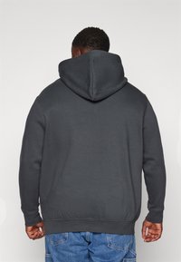 Sudadera gris oscuro con capucha ajustable, puños y dobladillo acanalados, de textura suave, llevada sobre unos jeans de mezclilla azul claro.
