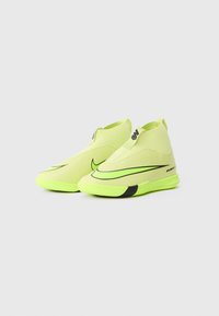 Zapatillas deportivas amarillo-verde con un diseño elegante, parte superior texturizada y un distintivo swoosh negro de Nike en el costado. Suela plana para un buen agarre.