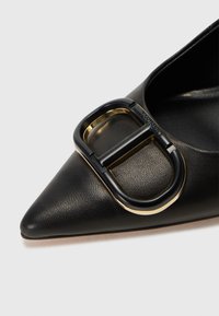 Scarpa nera in pelle a punta con dettagli di una fibbia chunky oro e nera sulla tomaia, con una finitura in pelle testurizzata.