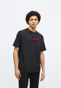 Čierne tričko s krátkym rukávom z bavlny s hladkou textúrou, s vystúpeným červeným logom "HUGO" cez hruď.