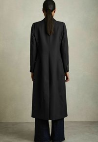 Palton negru croit, cu o siluetă lungă și dreaptă și umeri ajustați; prezintă mâneci lungi și nasturi la manșete; purtat peste blugi cu picioare largi.