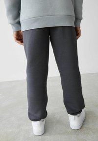 Grå sweats, lavet af blødt stof, tapered design, elastisk talje og sidesømme. Hvide sneakers med teksturerede såler.