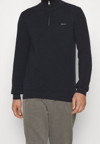 Navy blue zip-up pullover sweater made of textured knit fabric, featuring a high collar and small logo on the chest.