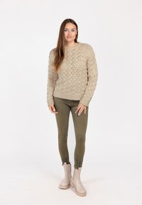 Beige gestrickter Pullover mit einem strukturierten Muster, grüne eng anliegende Hose und hellbeige Ankle Boots. Das Outfit hat gerippte Bündchen und Saum.