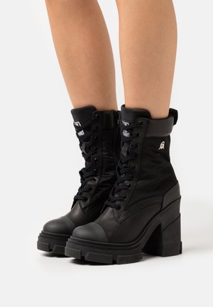 Bottines noires à design en matériaux mixtes, avec un bout en cuir, une tige en nylon et un talon haut épais. Comprend des lacets et un accent logo.