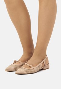 Nude Ballerinas mit spitzen Zehen, Netzstruktur und einem kleinen Riemen. Ausgestattet mit einer dekorativen Schleifenakzent und einem niedrigen Blockabsatz.