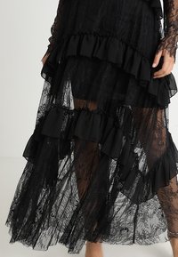 Abito nero in pizzo con balze a strati e texture trasparente, con maniche lunghe e silhouette fluida, che mette in risalto intricate trame.