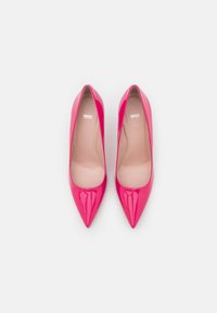 Chaussures à talons hauts en cuir verni rose avec un design à bout pointu et une finition lisse. Intérieur minimaliste avec un détail de marque à l'intérieur.