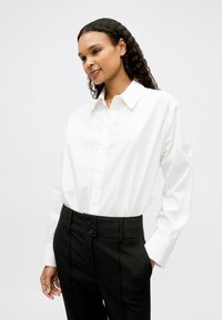 Balta pogājama krekla ar klasisku apkakli un garām piedurknēm, kopā ar augstās vidukļa melnām biksēm ar divām pogām un pielāgotu dizainu.