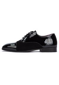 Zapato de vestir negro que combina charol brillante y gamuza mate, con punta afilada y cierre de cordones. Tacón plano.