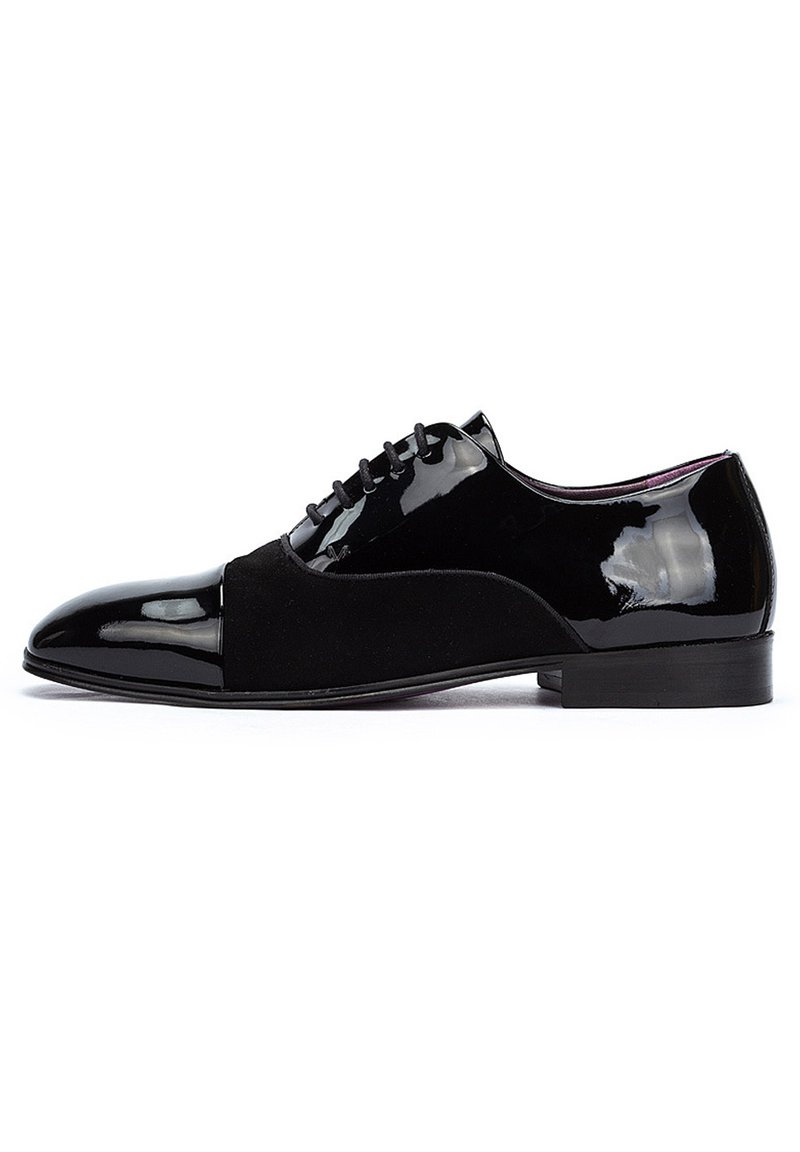 Zapato de vestir negro que combina charol brillante y gamuza mate, con punta afilada y cierre de cordones. Tacón plano.